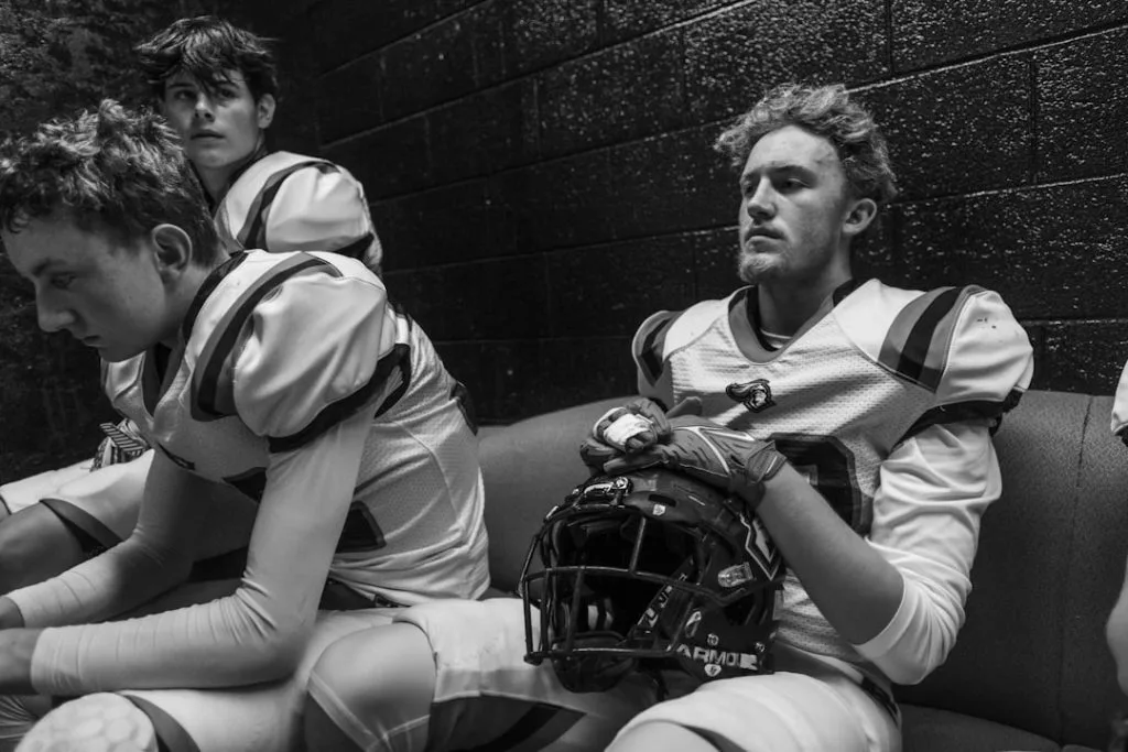 Football players in uniform sitting in a locker room
