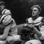 Football players in uniform sitting in a locker room