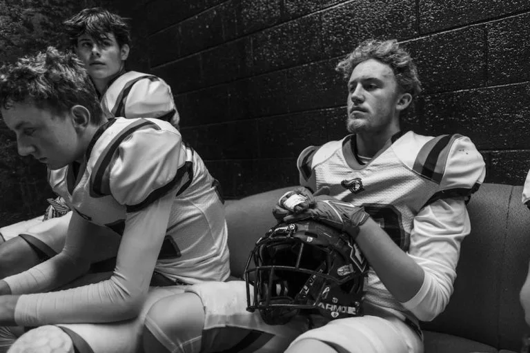 Football players in uniform sitting in a locker room