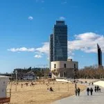 A group of people walking along a beach next to a tall building