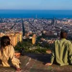 a group of people sitting on a ledge overlooking a city