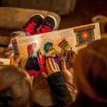 two childrens reading book while sitting on brown sofa